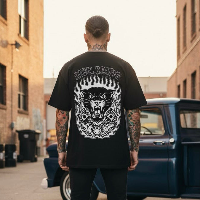 Man wearing a black t-shirt with a graphic design standing in an urban setting.