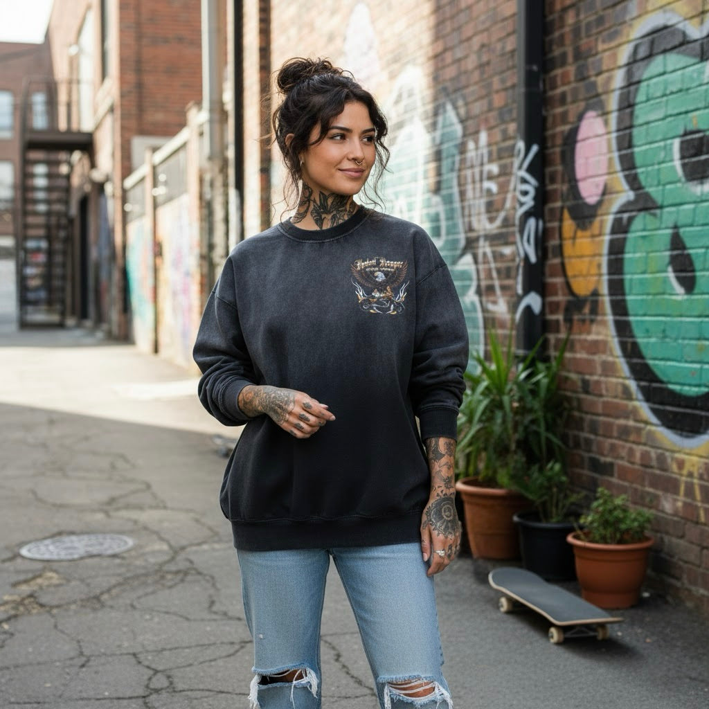 Woman wearing a black sweatshirt with a graphic design, standing in an urban setting with graffiti and plants.