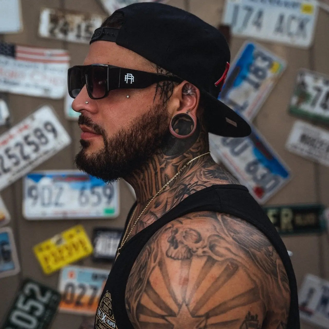 Tattooed man wearing Rebel Reaper Sunglasses with ear gauges showcasing stylish sunglasses