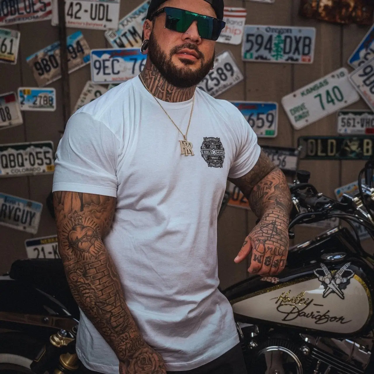 Tattooed man leaning on Harley-Davidson motorcycle wearing Rebel Reaper mens T-shirt in T-Shirts collection