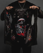 Person holding a black leather jacket with intricate designs on a dark background