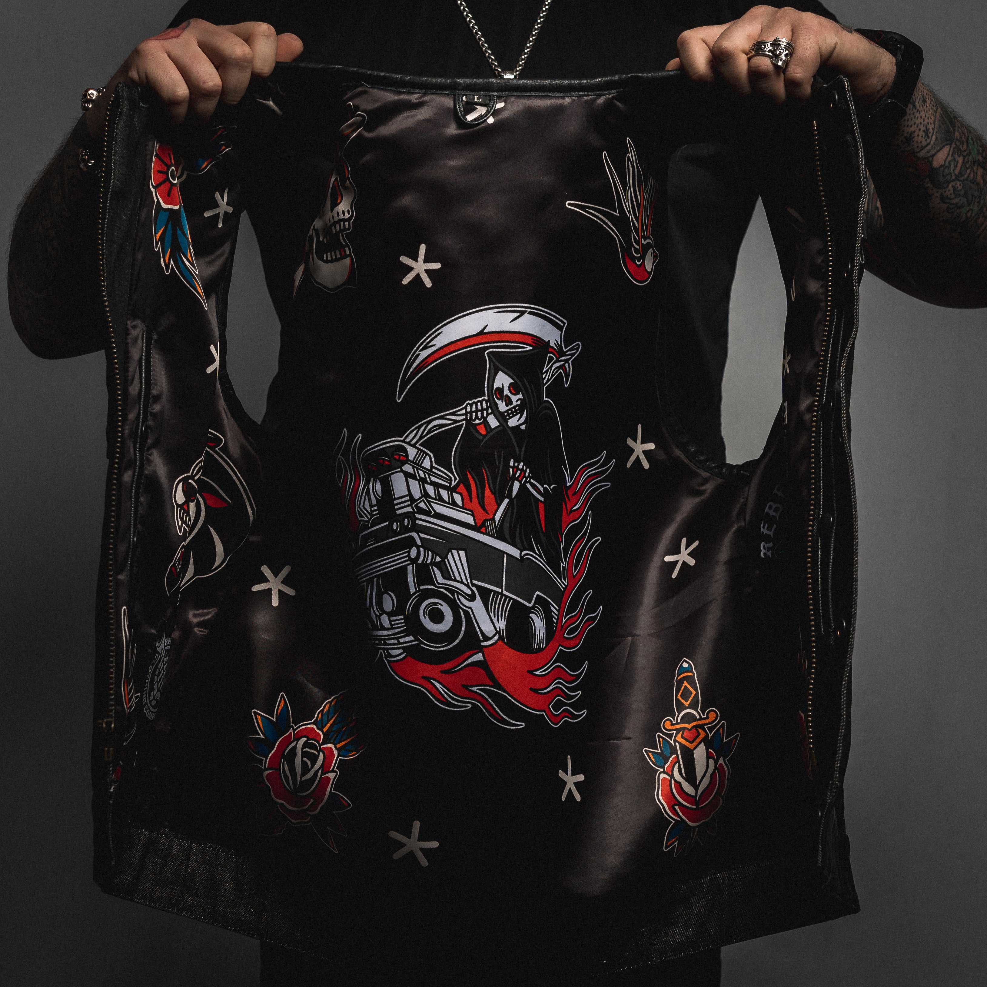 Person holding a black leather jacket with intricate designs on a dark background