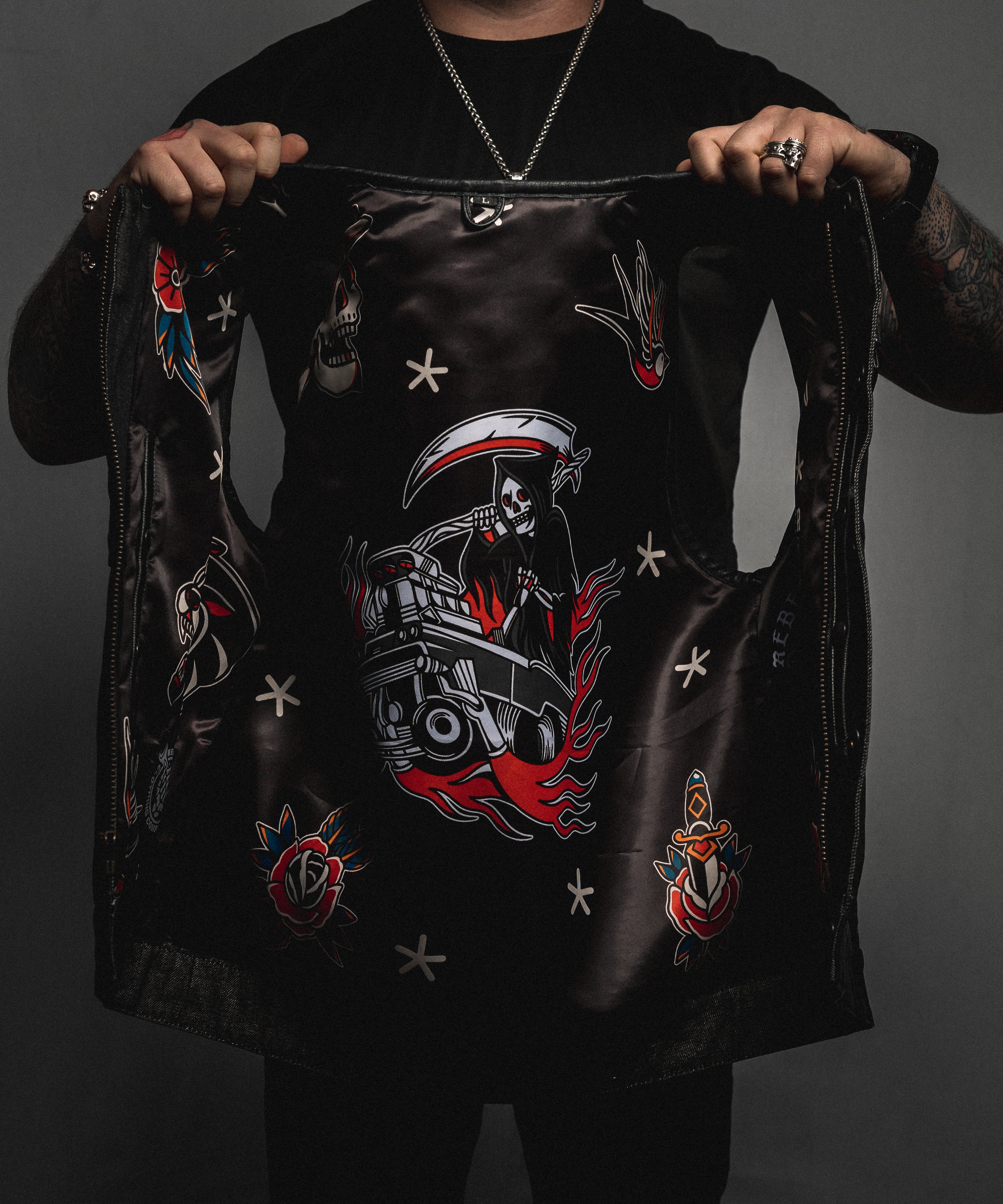 Person holding a black leather jacket with intricate designs on a dark background