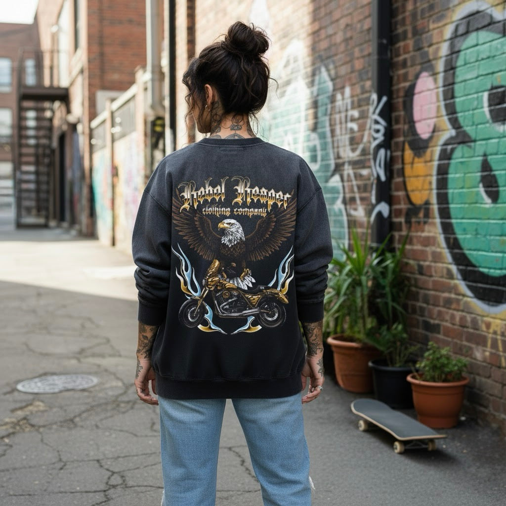 Person wearing a black sweatshirt with a graphic design, standing in an alley with graffiti on the wall.