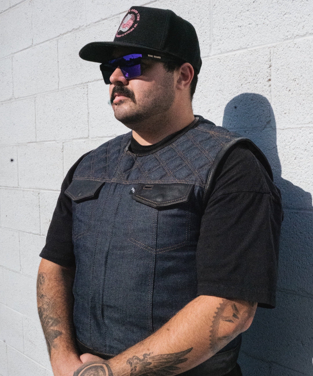 Man wearing a black vest and cap against a white brick wall