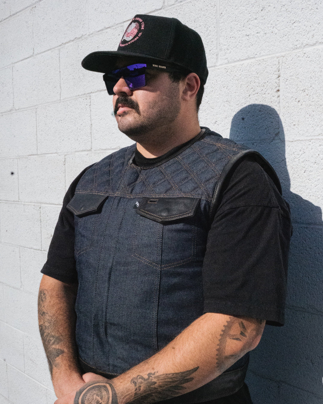 Man wearing a black vest and cap against a white brick wall