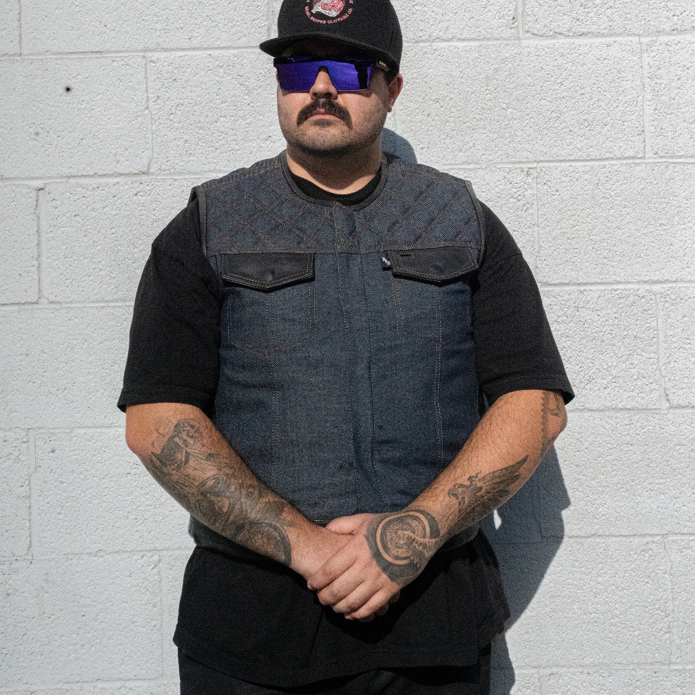 Man wearing a black vest and sunglasses against a light gray brick wall