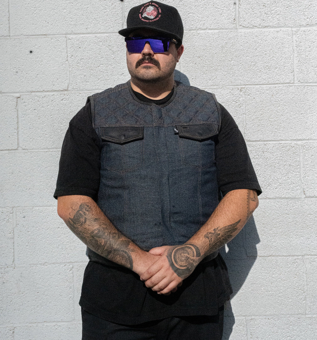 Man wearing a black vest and sunglasses against a light gray brick wall