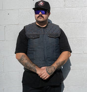 Man wearing a black vest and sunglasses against a light gray brick wall