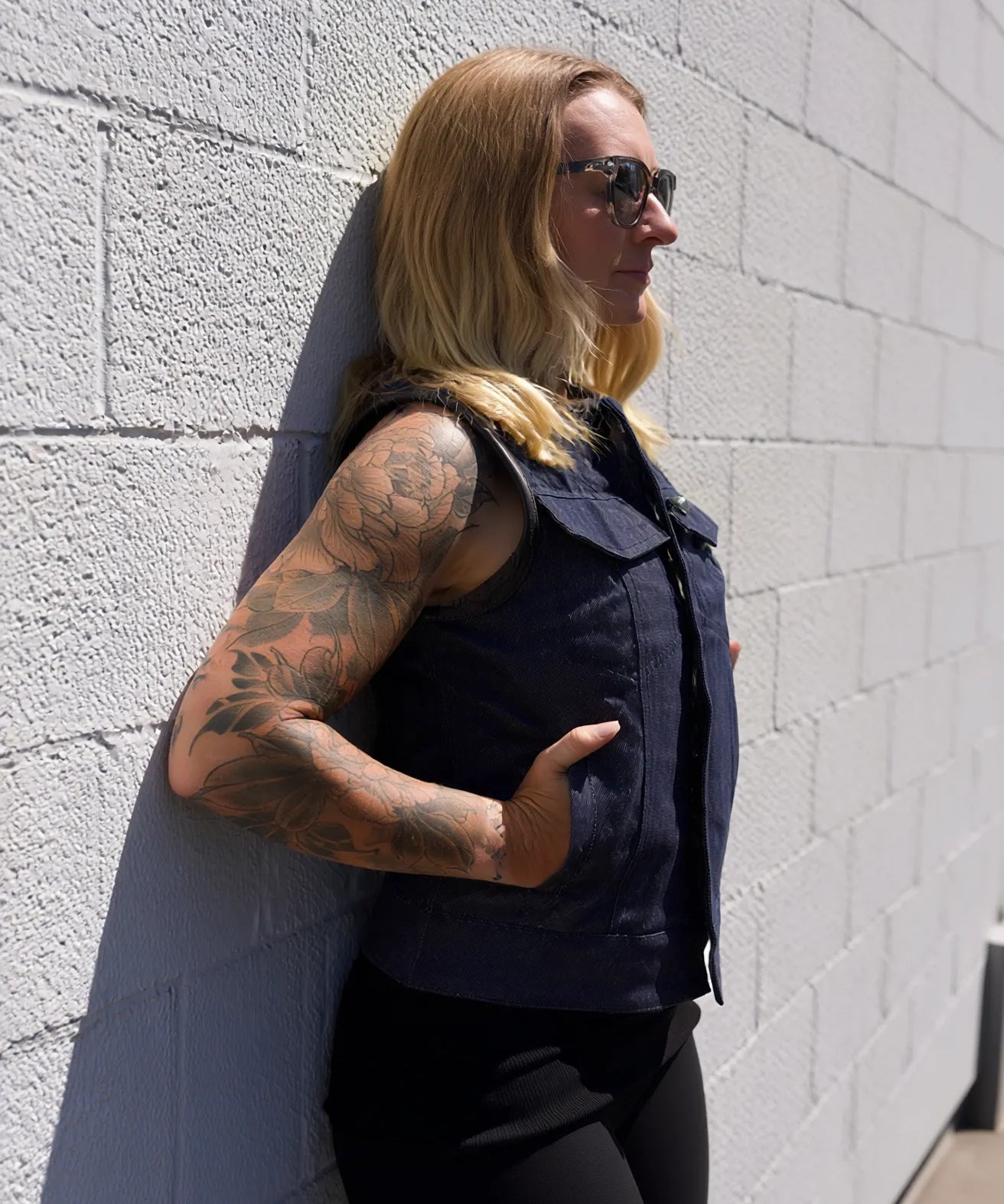Person wearing a sleeveless navy shirt and sunglasses, standing against a light gray wall.