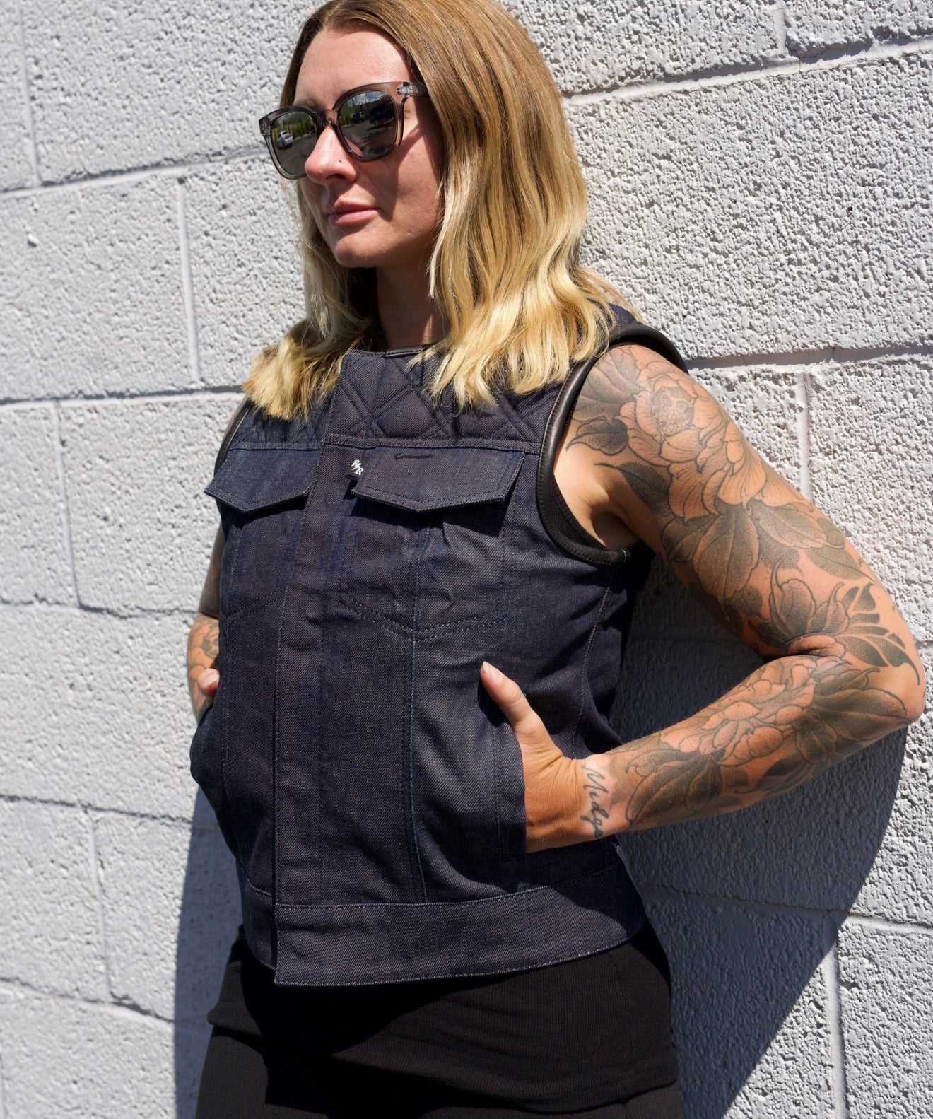 Person wearing a black sleeveless jacket against a gray brick wall