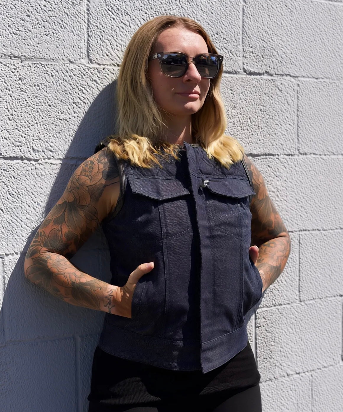 Person wearing a dark sleeveless shirt against a light gray brick wall
