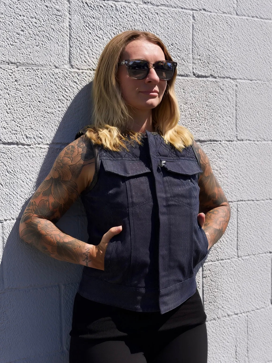 Person wearing a dark sleeveless shirt against a light gray brick wall