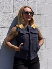Person wearing a dark sleeveless shirt against a light gray brick wall