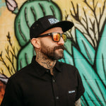 Man with tattoos wearing sunglasses and a black cap in Black Bamboo Button Up Shirt S/S with hidden collar buttons