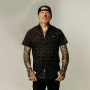 Tattooed man in patterned shirt featuring yellow metal hands and hidden collar buttons