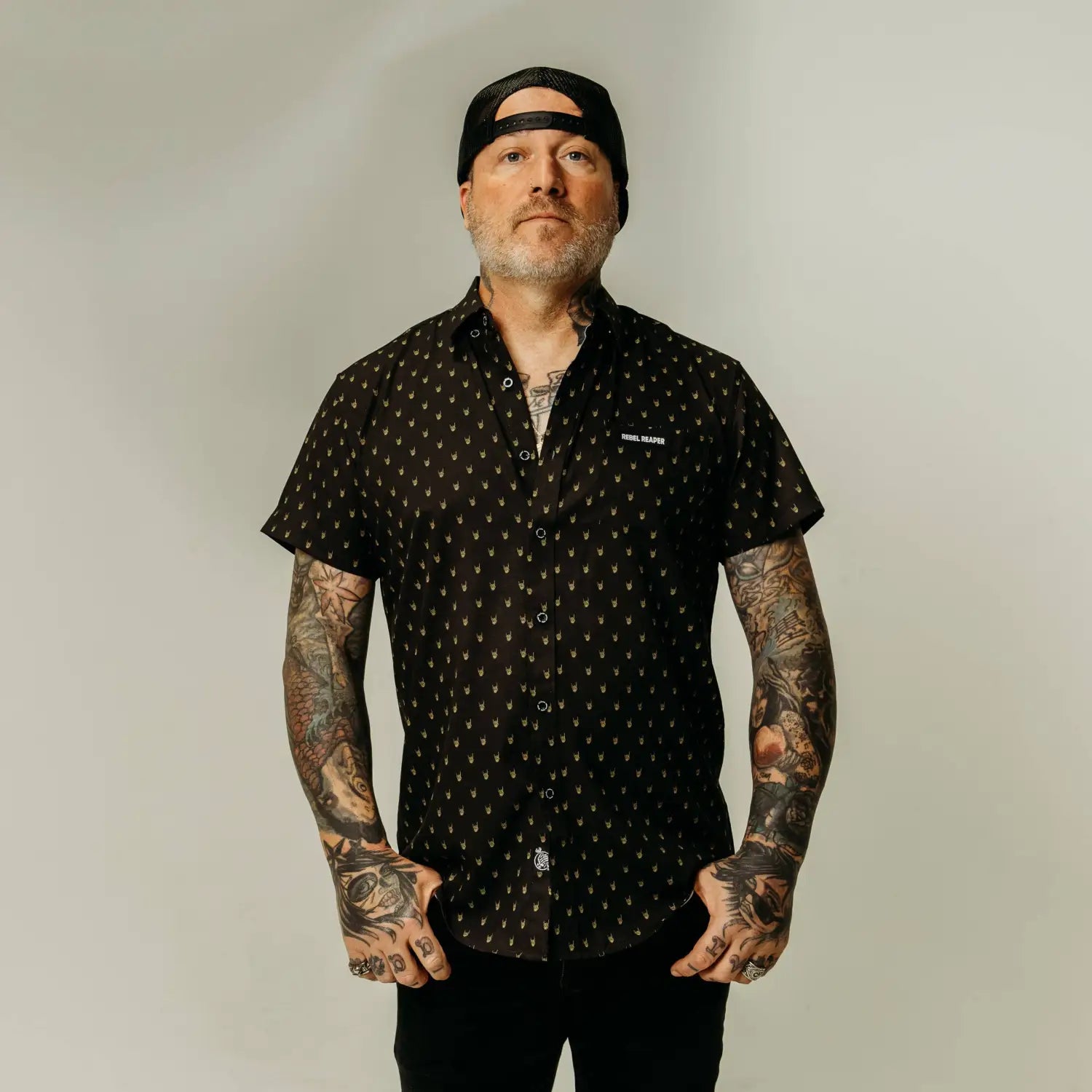 Tattooed man in patterned shirt featuring yellow metal hands and hidden collar buttons