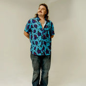 Man in patterned short sleeve button-up shirt with bold purple roses print