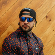 Man with sunglasses and patterned shirt from Hustler Wayfarer Sunglass Collection featuring interchangeable arms and signature rebel reaper style