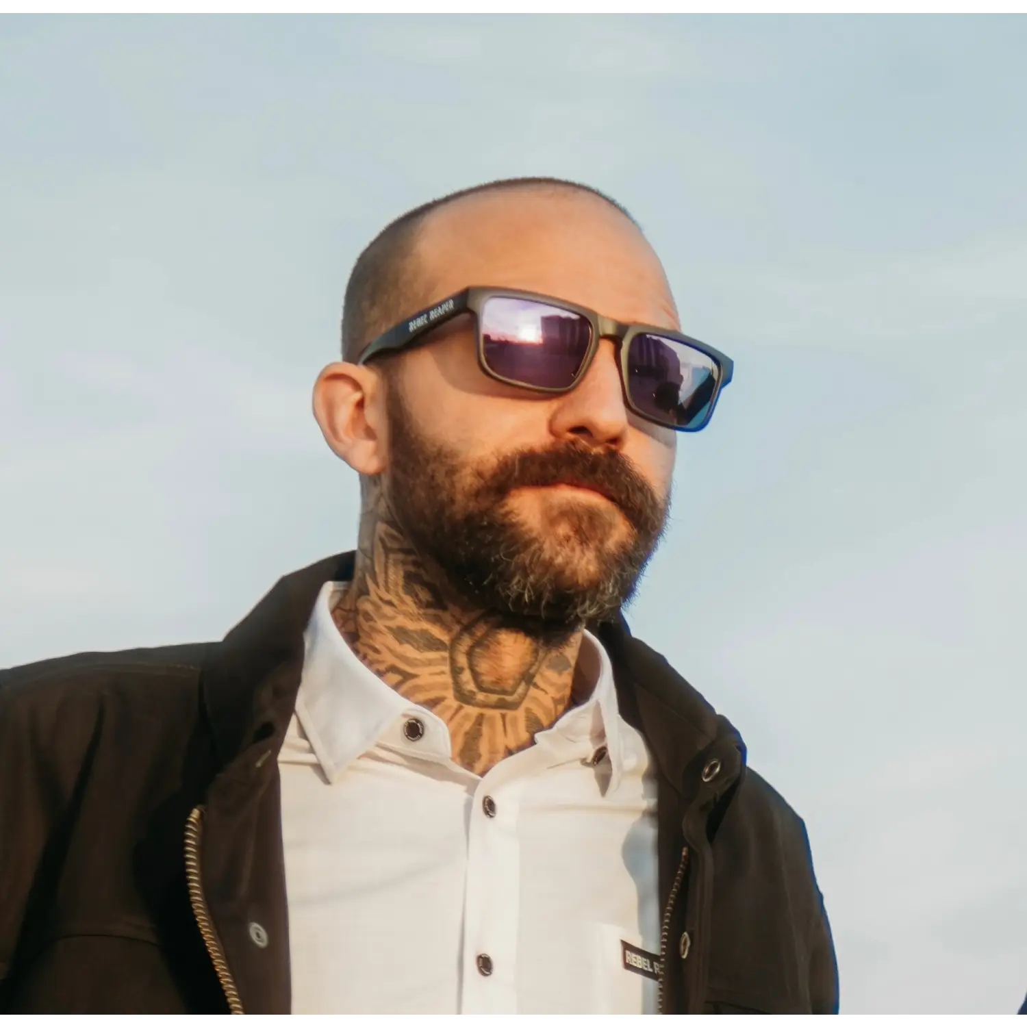 Bearded man with sunglasses and neck tattoo from Hustler Wayfarer Sunglass Collection featuring signature rebel reaper and interchangeable arms
