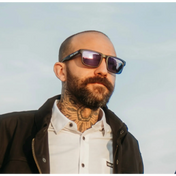 Bearded man with sunglasses and neck tattoo from Hustler Wayfarer Sunglass Collection featuring signature rebel reaper and interchangeable arms