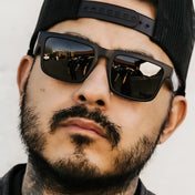 Man wearing sunglasses and a hat from Hustler Wayfarer Sunglass Collection with signature rebel reaper interchangeable arms