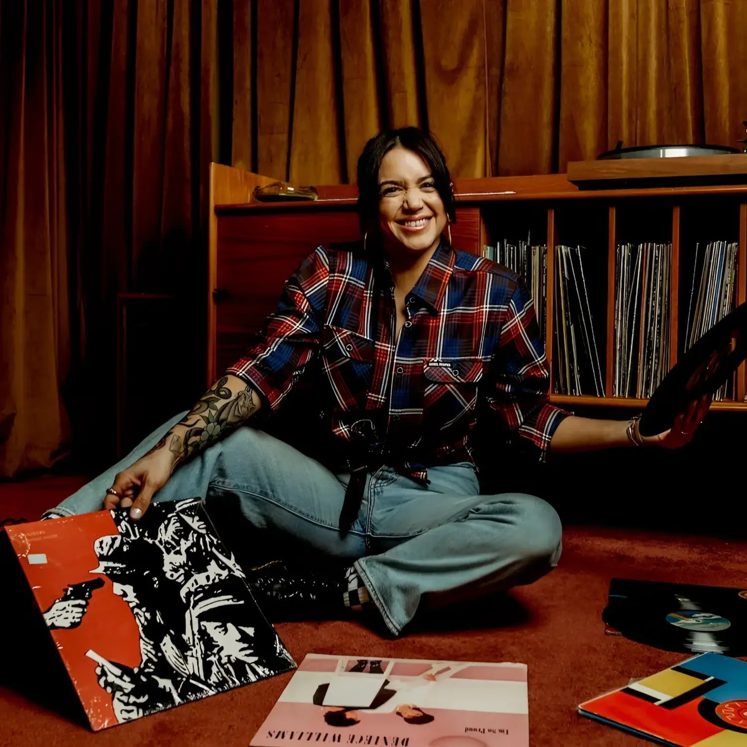 Person sitting on the floor surrounded by vinyl records in a room with wooden walls.