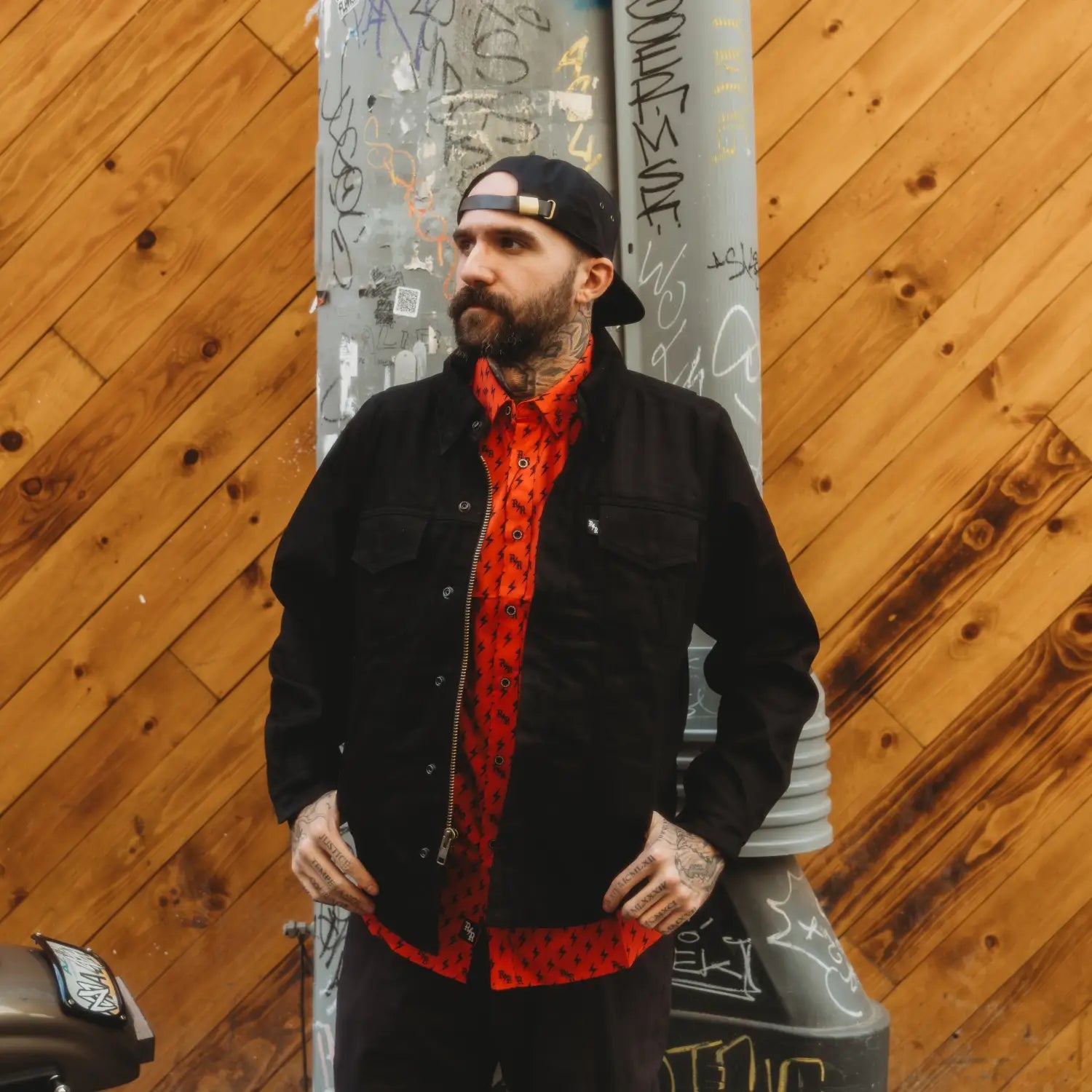Tattooed man in Black Jacket showcasing Red Iconic Bolts Button Up Shirt with hidden collar buttons