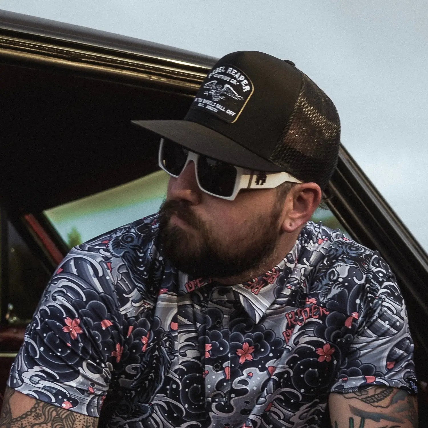 Bearded man in patterned shirt wearing Retro Squared Polarized Sunglasses with rebel reaper tattoo