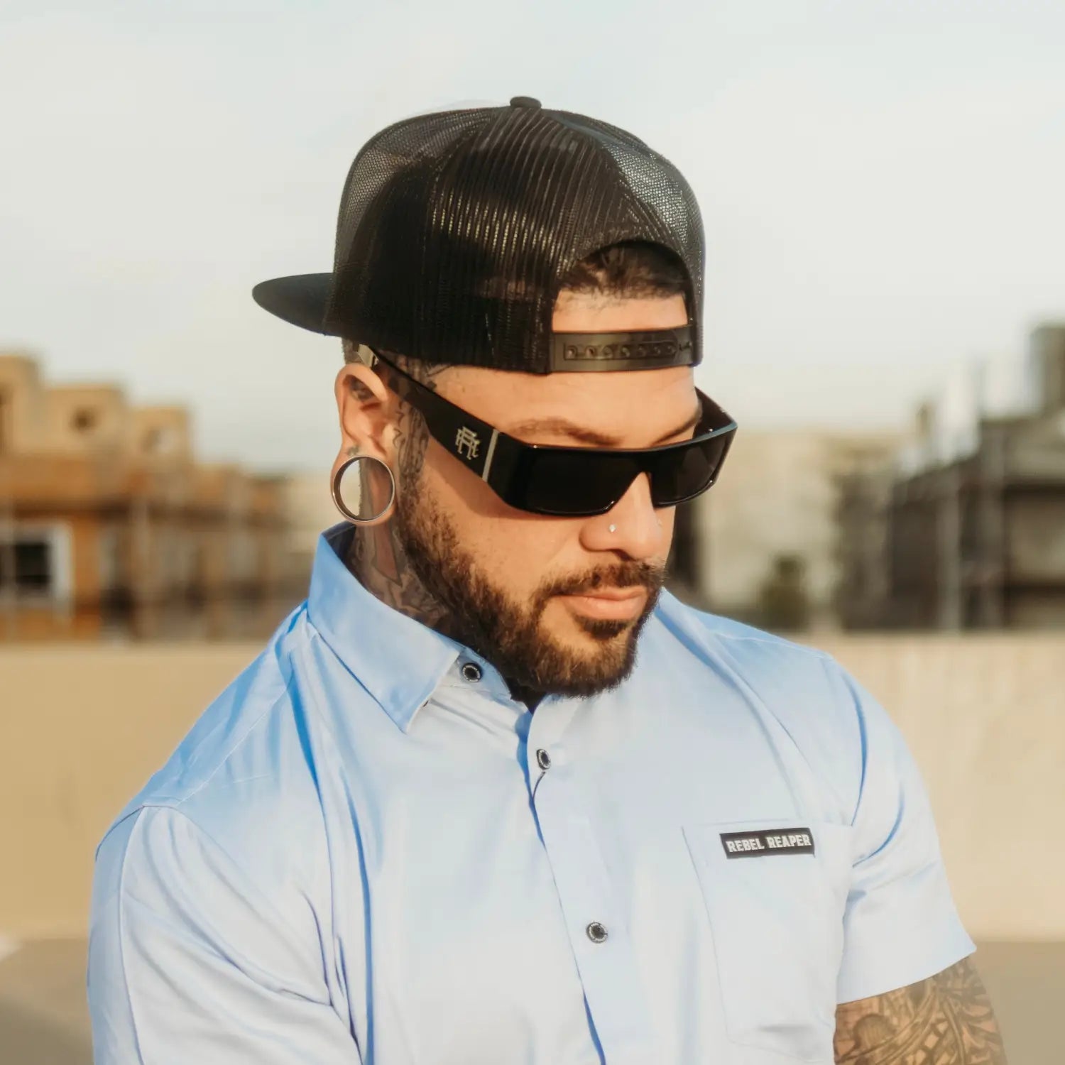 Man with tattoos, sunglasses, and a cap from the Slick Polarized Sunglass Collection featuring rebel reaper monogram and metal rebel reaper designs